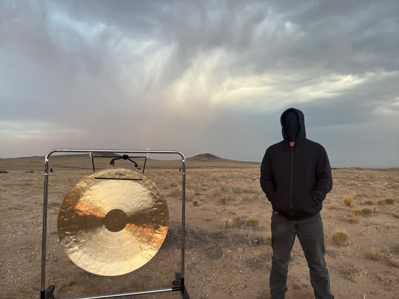 Gong Slayer beside a gong in open desert under a stormy sky