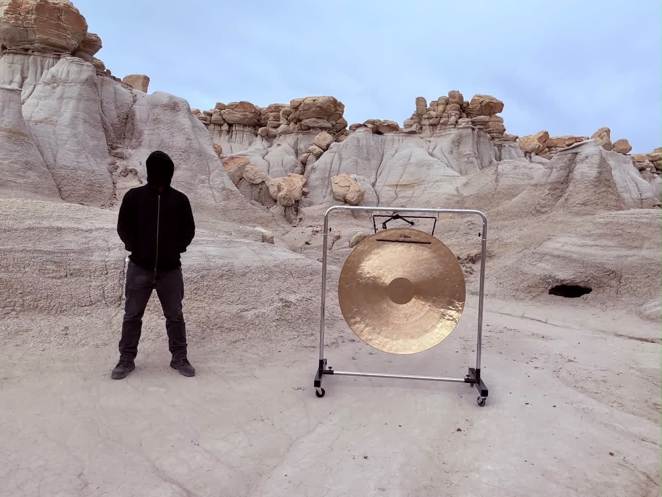 Gong Slayer beside a gong in front of pale rock formations