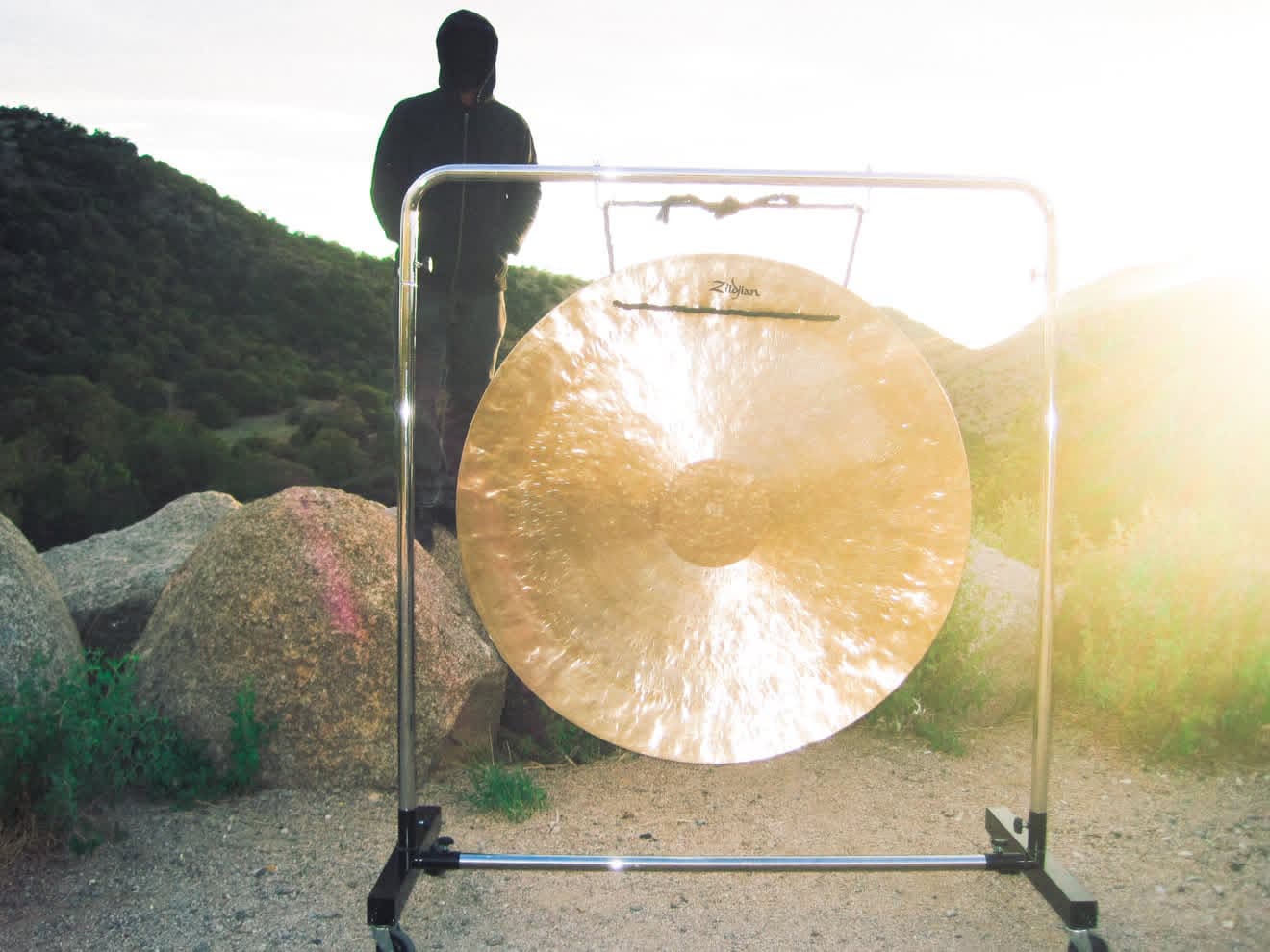 Gong Slayer in a black hoodie behind a gong on a rocky hillside